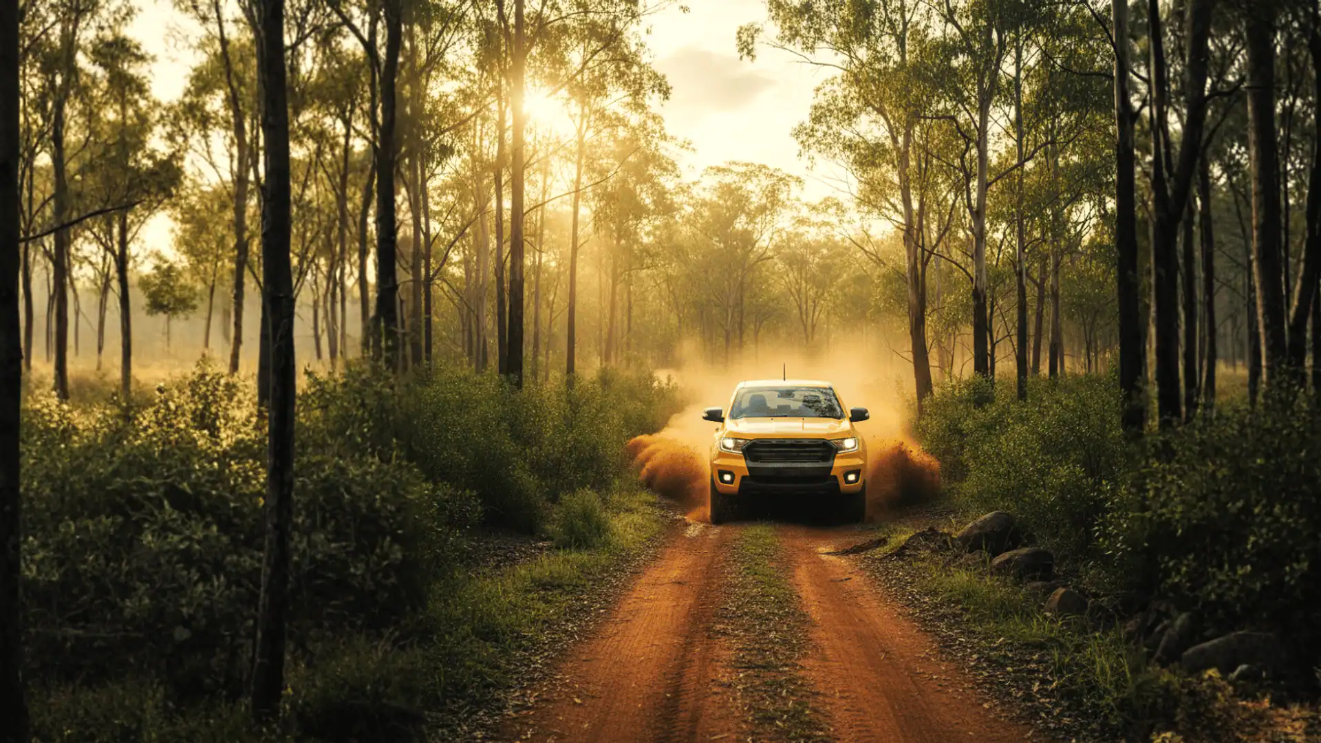 A yellow ute on a red-dirt bush track through gum trees.