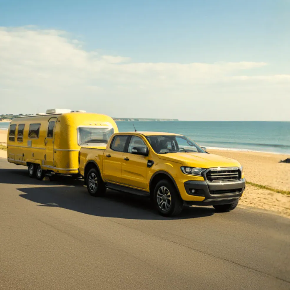 A yellow ute towing a caravan along a coastal road.